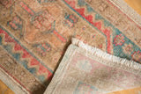 Vintage distressed Oushak rug corner showing low pile, white fringe, and woven back.