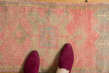 Distressed low pile of a vintage Oushak rug with blush pink, tangerine, and silver pattern.
