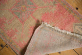 Distressed pink and beige vintage Oushak rug corner showing fringe and hand-knotted back.