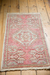 Distressed Oushak mat corner, blush pink field, ivory plant motifs, and even pile wear.
