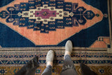 Vintage Oushak carpet with intricate stepped apricot medallion, dark navy field, and border.