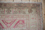 Oushak rug corner with faded raspberry red patterns, low pile texture, and fringe.