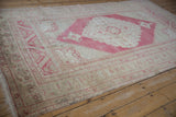 Low pile, intact selvage on corner of distressed Oushak rug with faded patterns.
