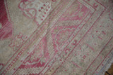 Faded raspberry red and sand patterns on a distressed vintage Turkish Oushak rug with fringe.