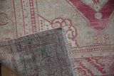 Distressed vintage Oushak rug corner, showing faded raspberry red pile, fringe, and hand-knotted reverse.
