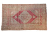 Vintage distressed Oushak carpet with a raspberry red medallion on a soft, time-worn beige field.