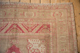 Corner detail of a distressed vintage Oushak rug showing the low pile, raspberry zigzag border, and intact selvage.
