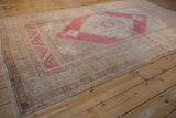 Angled perspective of a vintage distressed Oushak rug with a central raspberry red medallion.