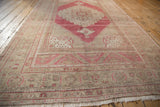 Angled view down the length of a distressed Oushak carpet showing its raspberry red and beige low-pile design.