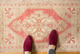 Distressed Oushak rug corner, featuring geometric pinwheel motif in pale brick red and ivory.