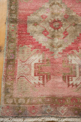 Distressed Oushak rug corner, highlighting pale cherry, blush, bronze tones, plant motifs, and fringe.
