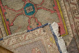 Corner of a vintage Distressed Oushak rug mat revealing original blue selvage, fringe, and low pile with blush and teal patterns.