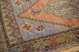 Distressed corner of Oushak rug featuring terra cotta, muted blue, and stepped geometric motifs.