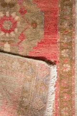 Distressed Oushak rug's low pile in blush and ivory, showing hand-knotted back and fringe.
