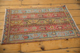 Distressed Oushak rug corner, fringed, with meandering vine motifs in red and blue tones.