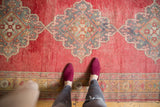 Distressed vintage Oushak runner with red field abrashes, Rococo-inspired medallion, and plant motif border.