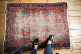 Vintage Lilihan Persian rug corner with worn red field, navy border, and ivory fringe.