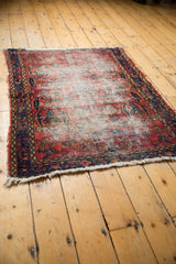 Vintage Lilihan rug corner displaying worn red field, deep navy border, and tattered fringe.