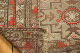 Antique Caucasian rug corner, hand-knotted geometric pile in silver, brick red, charcoal, and aged fringe.