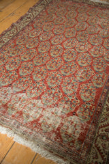 Vintage Hamadan rug end showing brick red boteh design, fringe, and worn pile with visible foundation.