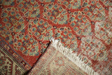 Vintage Hamadan rug corner with brick red boteh design, pile wear revealing foundation, and white fringe.
