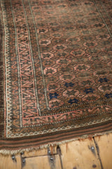 Corner of Vintage Belouch rug with secure side cord, geometric border, and tattered fringe.