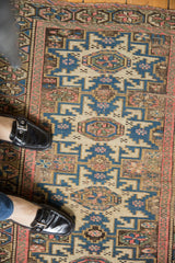 Vintage Caucasian rug's pale beige field, blue geometric patterns, and blush pinwheel motifs.