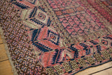 Close-up of antique Turkmen rug's fuchsia geometric tent motif, navy accents, and worn pile.
