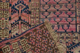 Folded fringed corner of antique Turkmen rug, showing fuchsia and navy geometric patterns with wear.