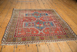 Cherry red field, blue geometric motifs, animal figures, and wear on vintage Caucasian rug with fringe.
