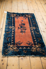 Antique Chinese Peking rug's apricot open field, central indigo floral motif, and beige border pattern.