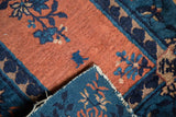 Corner of an antique Peking rug, showing hand-knotted structure, apricot pile, and indigo blue border.