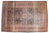 Antique Kermanshah carpet with an oversized scalloped medallion, dark navy blue field, intricate arabesques, and terracotta borders.