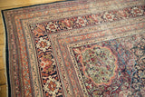 Angled view of the intricate terracotta and navy blue borders on an antique Kermanshah carpet.