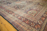 Angled view of an antique Kermanshah carpet highlighting the intricate borders and mostly even, low wear.