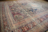 An angled view showing the intricate floral design and complex border system of an antique Persian Kermanshah carpet.