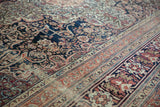 Intricate arabesques and low pile texture on an antique Kermanshah carpet's navy field and terracotta border.
