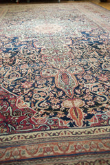 Low perspective across the antique Kermanshah carpet, showing even wear on its intricate navy and red patterns.