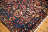 Vintage Baktiari carpet corner with dark navy border, cherry red blossoms, and visible pile wear.