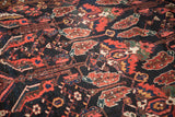 Close-up of Baktiari carpet, serrated leaf motifs in navy, cherry red, faint foundation showing.