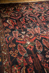 Vintage Baktiari carpet's dark navy field with serrated leaves, red blossoms, and visible wear.