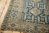 Corner of antique Shirvan rug, featuring geometric navy blue and sand patterns with visible wear.