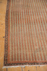Angled corner view of an antique Persian Senneh rug with even wear on its striped terracotta field.