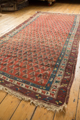 Bottom left corner of antique Caucasian runner with madder red boteh pattern, geometric border, and natural fringe.