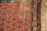 Madder red boteh, visible foundation, blue geometric border, aubergine selvage, and fringe.