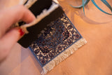 Miniature light blue rug coaster featuring traditional floral design and ivory fringe.