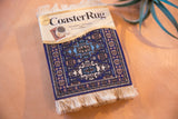 Ardabil Rug Coaster in packaging with blue, purple, ivory geometric design and fringe.