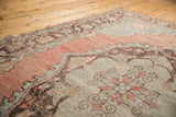 Distressed Oushak carpet with faded blush, pale green, and charcoal medallion details.