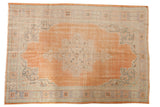 Distressed vintage Oushak rug with soft apricot field, faded floral medallion, pale blue border, 6'5