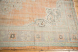 Distressed Oushak carpet corner, revealing worn pile, apricot blush field, and sea foam border.